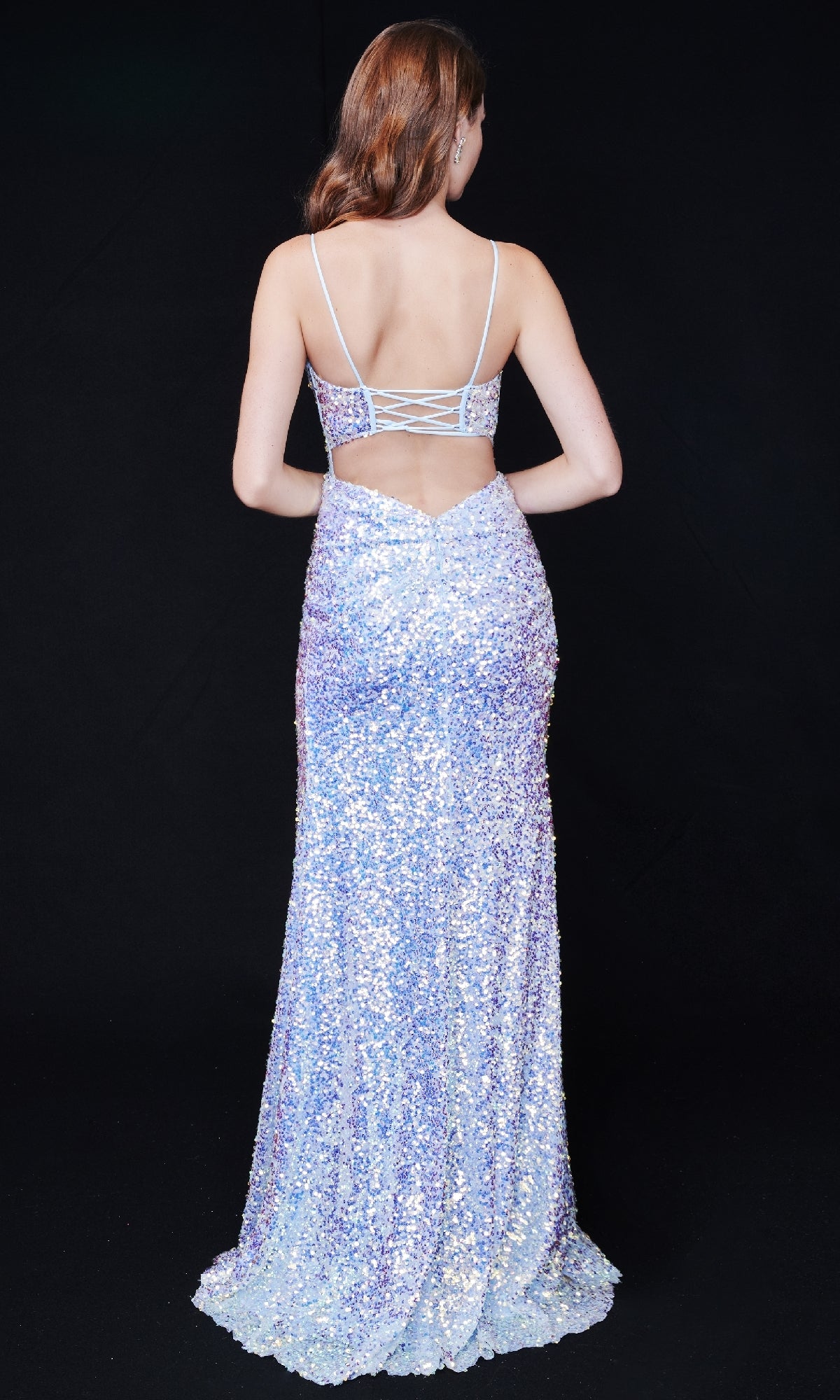 A woman faces away in the Nina Canacci 4406, a long sequin formal dress with thin straps, open back, and high side slit, set against a plain black background.